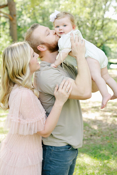 Father holding baby kissing it's cheek while mom smiles