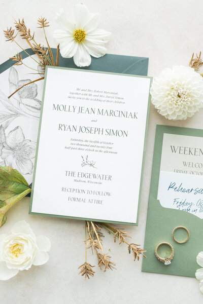 A black and white custom wedding invitation suite featuring a debossed invitation with wedding rings on it and a details and RSVP card by alyssa amez design custom wedding stationery and signage designer against a white background.