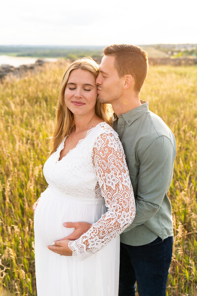 Couple kissing and holding onesie for their pregnancy announcement photos