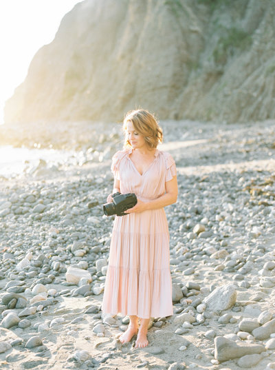 Alice Thigpen on a beach holding her camera in a pink dress