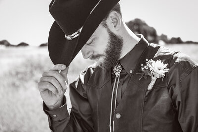 groom holding his cowboy hat in black and white