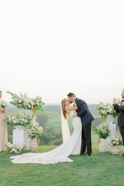 Beautiful wedding ceremony at Granite Links in Quincy Massachusetts, featuring a stunning floral arrangement as the backdrop. The bride and groom exchange vows in an intimate outdoor ceremony, surrounded by lush greenery. Felisha, a destination wedding photographer based in New England, captures timeless moments at weddings in Massachusetts, New England, and worldwide locations.