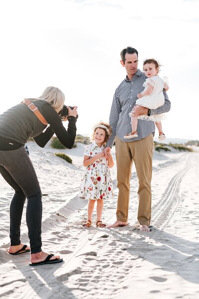 a photographer takes photos on the beach in San Diego of a dad and his two daughters