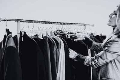 black and white image of a woman selecting clothes from a rack during a styling session