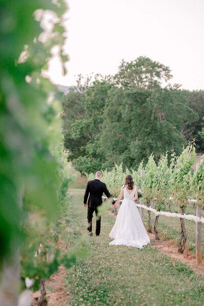 Calm photo of a bride and groom holding hands in a Virginia vineyard wedding venue.