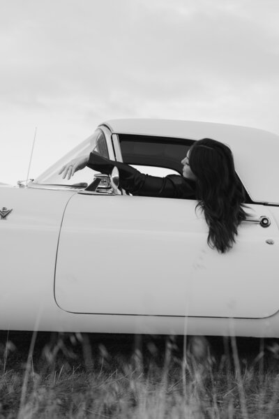 Black and white editorial portrait of a woman stretching her arm out a car window, seated in a vintage vehicle. Artistic photography in Greenville, South Carolina by Dani Lacey Photographs.