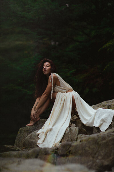 red head woman in a long white gown sitting near the water at lynn canyon
