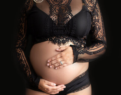 Mom holding pregnant belly in black lace.