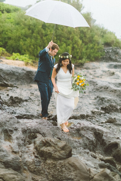 groom holds umbrella for the bride as she walks along the rocks at an oregon beach