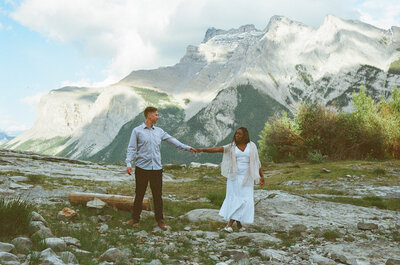 bride and groom hold hands in front of mountain in Banff