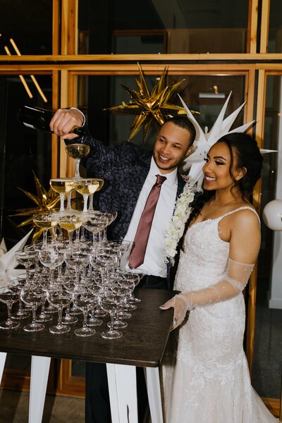 A bride and groom pour a champagne tower at their wedding.