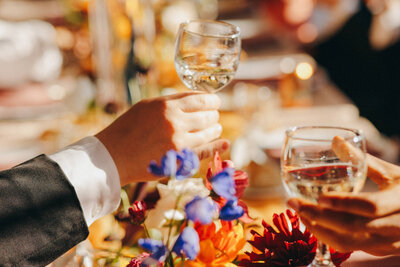 a colorful image of people's hands holding champagne glasses to cheers