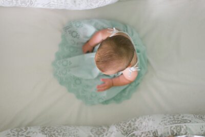 Top view of a baby sitting in a crib wearing a green lace dress, symbolizing innocence, new life, and the cherished gift of adoption.
