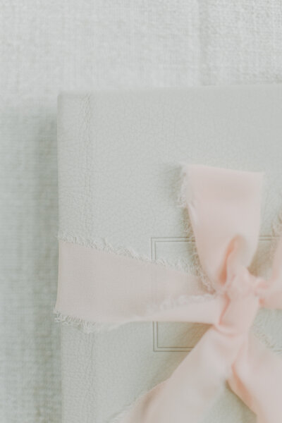 A close up photo of a light tan leather photo album wrapped in a pink bow