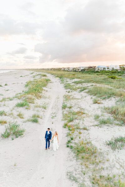 drone photo of bride and groom walking on the beach at sunset