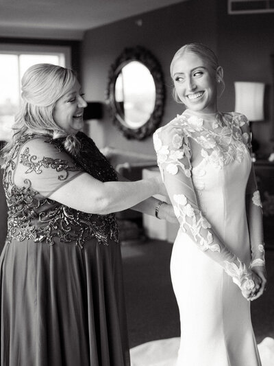 Black and white photo of bride's mother zipping up her dress