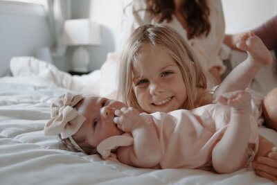Sibling cuddling a newborn baby on a bed