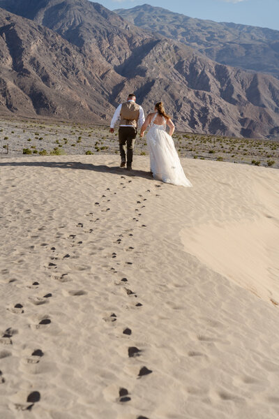 A couple walks beneath palm trees in wedding attir