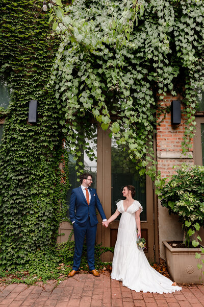 Couple holds hands in front of ivy wall at The Mae District in Chicago, IL.