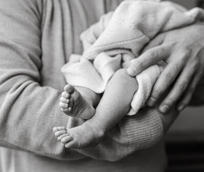 Dad is holding the newborn and focusing on their feet during in-home newborn session with Allison Krogness Photography.