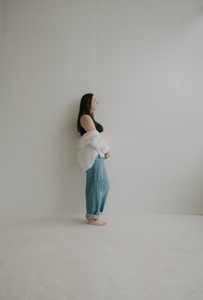 A portrait of a pregnant woman. She leans against the white walls of a modern studio in Batavia, NY. Photo by Dash and Boheme Photography. 
