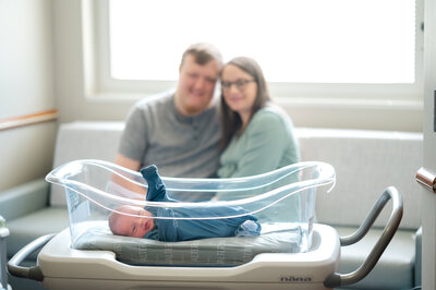 Baby lays in crib at the hospital while parents look lovingly in the background. Photo taken during their fresh 48 session in Athens by Amanda Touchstone