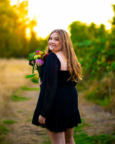 A colorful portrait of a Lake Washington High School girl. She is sitting in front of blue flowers in Federal Way, Washington. She is wearing a floral blue crop top and white skirt as an outfit for her senior photos.