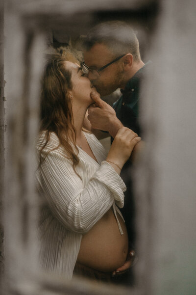 A pregnant mother wearing a gorgeous gown holding her belly while her husband holds her chin up to gaze at him. 