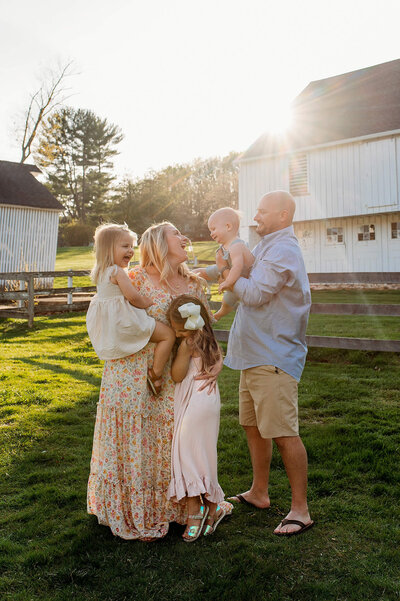 Family laughing in front of white barn at sunset