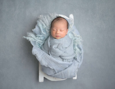 Beth Benecki of E. Benecki Photography captured this image of a sleeping newborn wrapped in light blue blankets and fluffs.