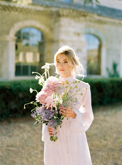 Beautiful bride holds floral bouquet outside chateau