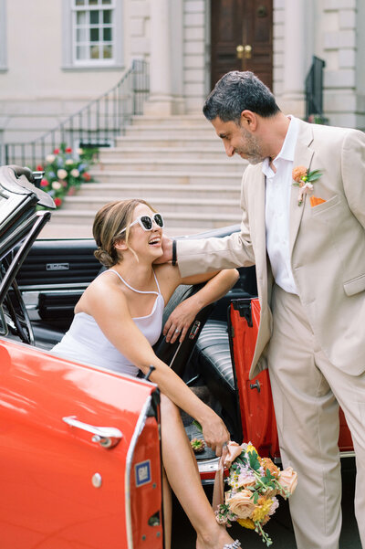 During couple's portraits, a husband and wife lounge in a red antique car at their DMV wedding