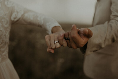Detail shot of bride and groom's rings on their fingers while they pinky promise.