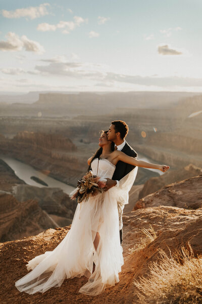 Bride and groom embracing over desert canyon