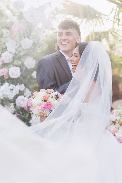 Bride with a long veil laughing with Groom  on their wedding day