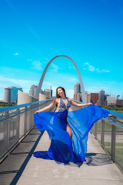 Teenage girl in blue evening gown poses for senior portraits under the arch in St Louis