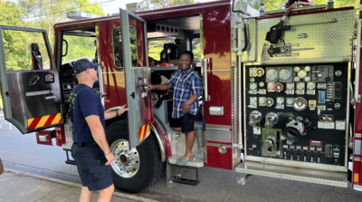 Young boy standing in firetruck next to a fire fighter at the NWA Black Heritage Juneteenth Celebration