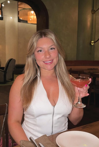 A girl with long blonde hair all dressed up having drinks with friend in celebration of her brand launching. 