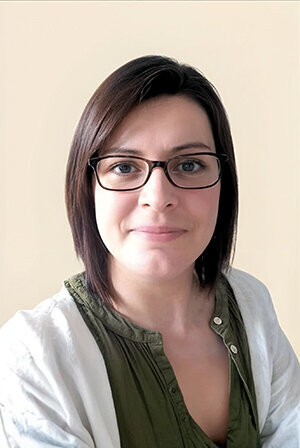 Portrait d'Aurore, cheveux mi-longs bruns, portant des lunettes et un gilet blanc, cliente audit de communication.