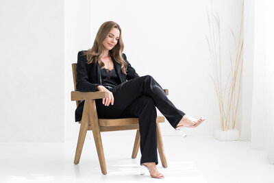 žena v černém kostýmku sedí na hnědém křesle a dívá se dolů