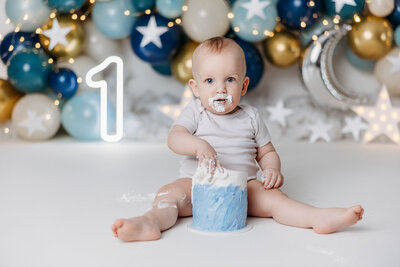 image of a 1 year old birthday boy smashing his cake in front of a space theme balloon garland and stars cake smash session
