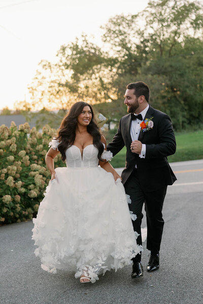 Bride in a fairytale ballgown with long, soft waves walks hand in hand with her groom — romantic wedding hair by Klover Beauty in Maryland.