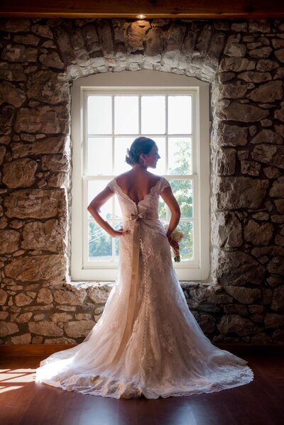 Bride stands in front of window inside rustic, rock wall room