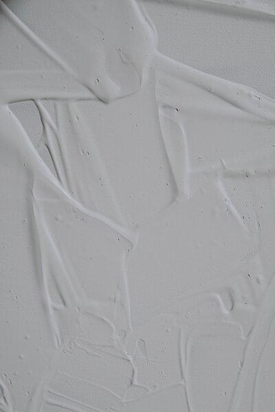 A close-up image of white paint or a similar thick substance spread unevenly on a smooth surface. The texture shows visible streaks, ridges, and small air bubbles, creating an abstract pattern with varying depths and shades of white.