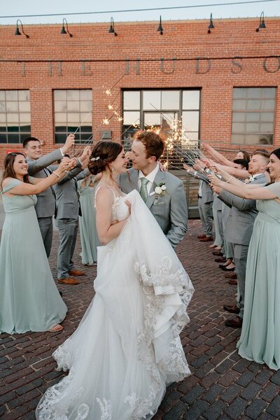 Bride and groom smiling about to kiss at the end of their wedding exit with the bridesmaids and groomsmen holding sparklers up