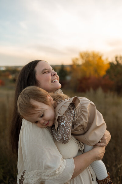 Owner of Beanie Bear Photography  holding her daughter against a sunset.