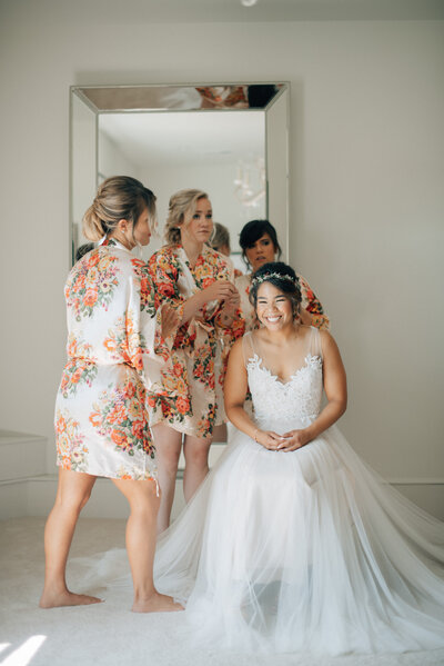 Bride sits in the getting ready room of The Palace Event Center while her bridesmaids fix her hair.