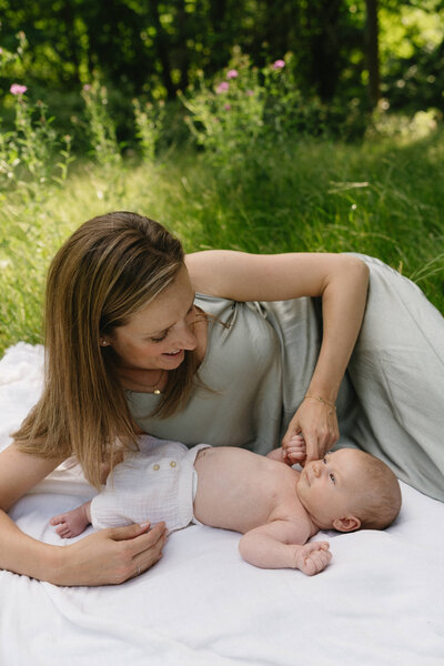 Foto van moeder die op een dekentje ligt in het park en kijkt naar haar newborn baby.