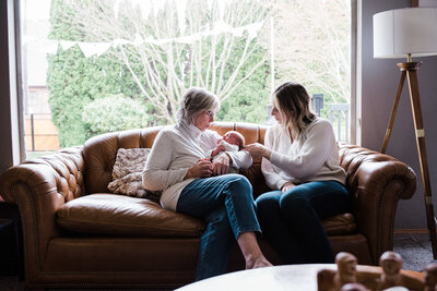 Grandma holding her grandson on couch with her daughter in mid century modern decorated home for newborn family photos
