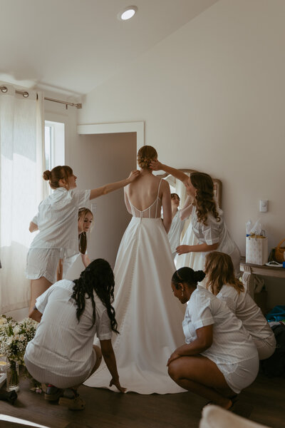 Bride in bridal suite with bridesmaids adjusting hair and dress.
